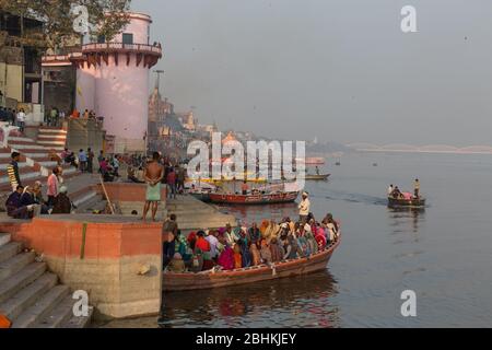 Ein Blick auf den Fluss Ganges bei Dämmerung im Sommer in der Nähe von Varanasi, Indien. Leute, die abends in Booten fahren, um die Aussicht auf Ghats am Flussufer zu sehen Stockfoto