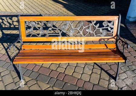 Eine dekorative Bank von Hand aus Schmiedemetall in Form von Blättern und einem Holzsitz, auf einem Pflasterstein stehend. Stockfoto