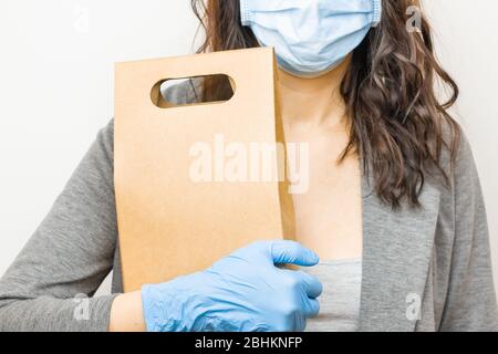 Lieferservice während der Quarantäne der Coronavirus-Pandemie aus dem Online-Shop. Kurier in Schutzmaske und blauen Handschuhen hält Papptasche Stockfoto