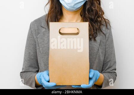 Der Liefermann hält eine Papiertüte mit Kopierraum in medizinischen Handschuhen und Schutzmaske. Online-Shopping während der Quarantäne. Stockfoto