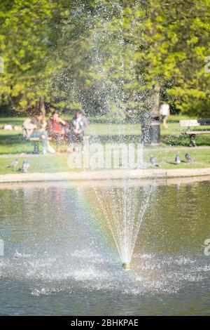 Drei Mädchen (außer Fokus) auf Bank im Pinner Memorial Park, Großbritannien, durch den Wasserbrunnen im See genommen. Stockfoto