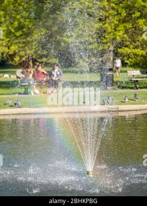 Drei Mädchen (außer Fokus) auf Bank im Pinner Memorial Park, Großbritannien, durch den Wasserbrunnen im See genommen. Stockfoto