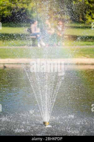 Drei Mädchen (außer Fokus) auf Bank im Pinner Memorial Park, Großbritannien, durch den Wasserbrunnen im See genommen. Stockfoto