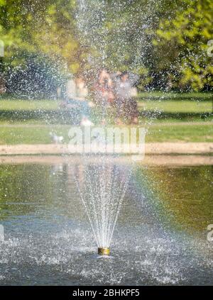 Drei Mädchen (außer Fokus) auf Bank im Pinner Memorial Park, Großbritannien, durch den Wasserbrunnen im See genommen. Stockfoto