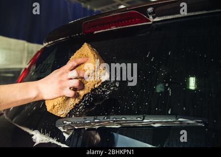 Autotür aus Glas mit Schaumstoff und eine Hand mit Schaumschwamm Stockfoto
