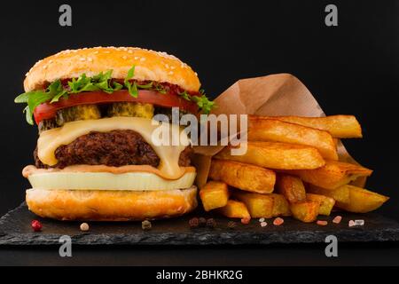 Ein großer klassischer Hamburger mit pommes frites auf schwarzem Steinteller auf schwarzem Hintergrund und Platz für Text Stockfoto