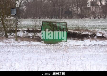 Ein alter, grün bemalter Metallschuppen aus Corugated sitzt in einem Feld von Bauern, das mit leichtem Schnee bedeckt ist. Stockfoto