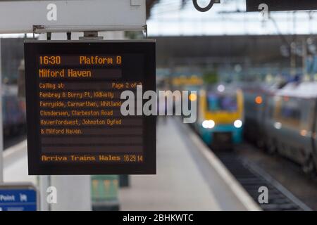 Infopoard für die Zugabfahrt am Bahnhof Manchester Piccadilly mit einem Zug im Hintergrund Stockfoto