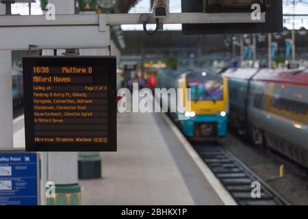 Infopoard für die Zugabfahrt am Bahnhof Manchester Piccadilly mit einem Zug im Hintergrund Stockfoto