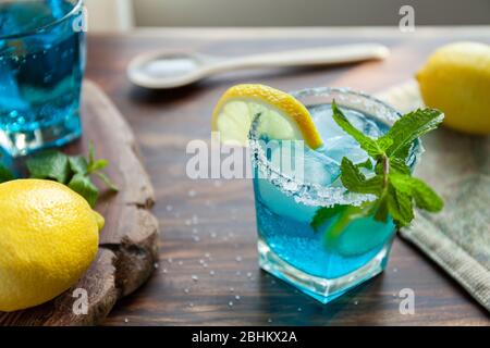 Alkoholischer Cocktail auf einem Holztisch umgeben von Zutaten wie Zitrone, Salz, Zucker, Eis Stockfoto