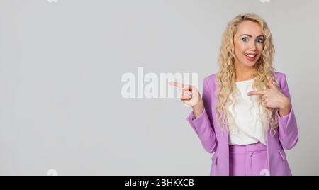 Fasziniert, charmant, blonde Frau, überraschte Dame, überrascht, offenen Mund, zeigt die Richtung nach links, glücklich, hebt ihre Augenbrauen. Wow, fantastisch Sagen Sie mehr Stockfoto