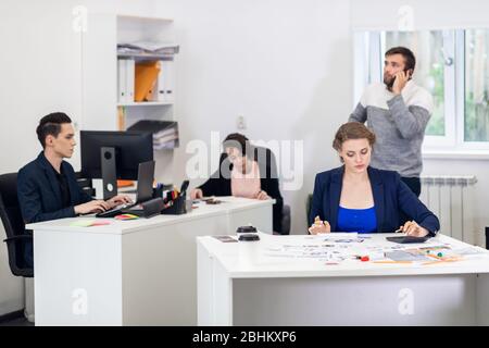 Büromitarbeiter in einem offenen Raum, verschiedene Dinge tun, Kollegen chatten, Projekte diskutieren, an PCs arbeiten, etwas Papierkram erledigen. Coworking-Kontra Stockfoto