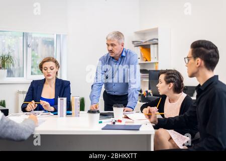 Gruppe junger Geschäftsleute, die ein Treffen mit ihrem Chef haben. Vielfältige Gruppe von Mitarbeitern diskutieren neue Entscheidungen, Zukunftspläne und Strategien. C Stockfoto