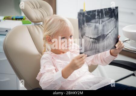 Ein kleiner Patient untersucht eine Röntgenaufnahme von echten Zähnen in einer Zahnarztpraxis. Stockfoto