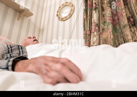 Bedeckt mit einer Bettdecke, tragen Schlafanzug in einem Krankenhausbett unten in seinem Haus. Stockfoto