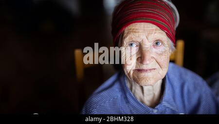 Porträt einer älteren Frau, die vor dunklem Hintergrund auf die Kamera schaut Stockfoto