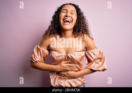 Junge schöne Frau mit lockigen Haaren tragen Casual T-Shirt über rosa Hintergrund lächelnd und lachen hart aus laut, weil lustig verrückt Witz Stockfoto