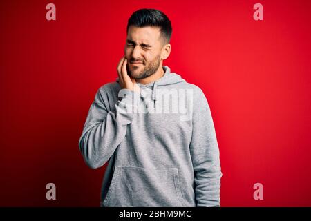 Junge gut aussehende Sportler tragen Sweatshirt über isoliert roten Hintergrund berühren Mund mit Hand mit schmerzhaften Ausdruck wegen Zahnach stehen Stockfoto