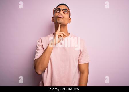 Schöner afroamerikanischer Mann mit lässigem T-Shirt und Brille über rosa Hintergrund Denken konzentriert sich auf Zweifel mit Finger auf Kinn und Blick Stockfoto