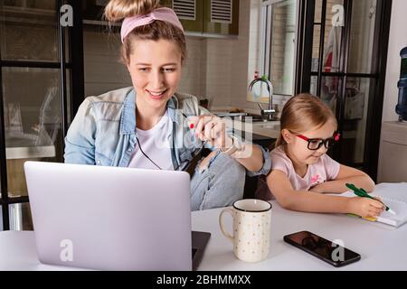 Geschäftsfrau mit Laptop in der Küche. Kind macht Hausaufgaben. Familienleben während der Sperrung des Coronavirus. Bleiben Sie während des covid-19-Konzepts zu Hause. Online Stockfoto