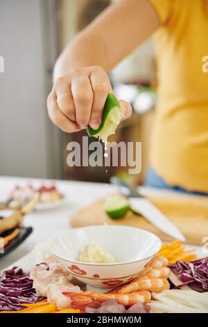 Frau quetscht Limettensaft in eine Schüssel mit Dip-Sauce für Garnelen und Gemüse Stockfoto