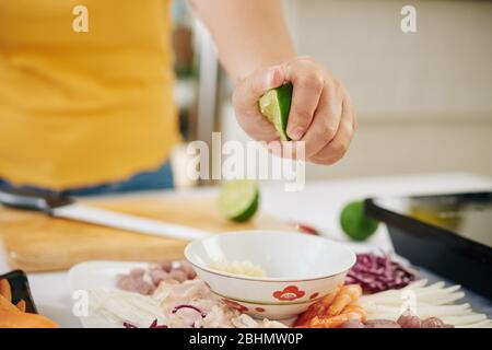 Hand der Frau quetschen Limettensaft in kleine Schüssel, wenn Dressing für Salat machen Stockfoto