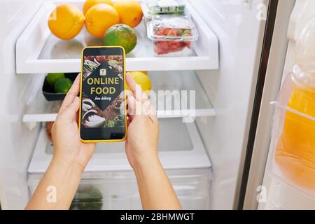 Frau überprüft Kühlschrank und Bestellung von Lebensmitteln über mobile Applciation, die kostenlose Lieferung während der Quarantäne bietet Stockfoto