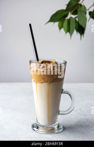 Dalgona Kaffee in einem hohen Glas mit Stroh auf weißem Hintergrund. Seitenansicht Stockfoto