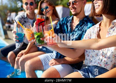 Ansicht schließen. Freunde klirren Gläser mit frischen bunten Cocktails sitzen am Pool an sonnigen Sommertag. Die Leute toasten Getränke an Stockfoto