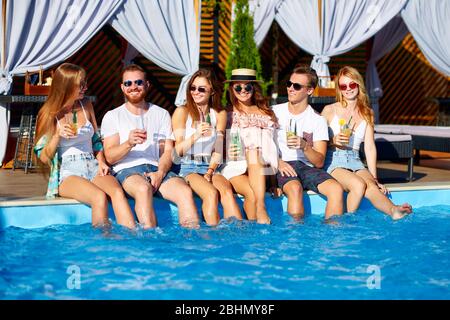 Eine Gruppe von Freunden, die am Pool Spaß haben, und am sonnigen Sommertag am Pool Gläser mit frischen Cocktails anklickend. Menschen stoßen an Stockfoto