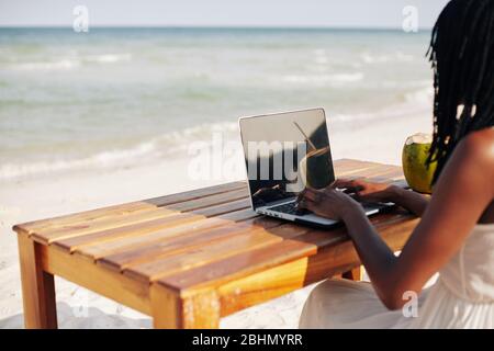 Freiberufliche oder bloggerhafte Frau, die am schönen Strand am Tisch sitzt und am Laptop arbeitet Stockfoto