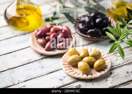 Vielfalt von schwarzen und grünen Oliven und Olivenöl in Schüsseln auf weißem Hintergrund Nahaufnahme Stockfoto