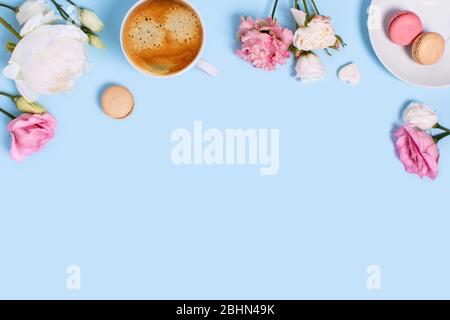 Blauer Hintergrund mit Makronen und einer Tasse Kaffee umgeben von Pfingstrosen und Rosen. Draufsicht mit Platz für den Text. Stockfoto
