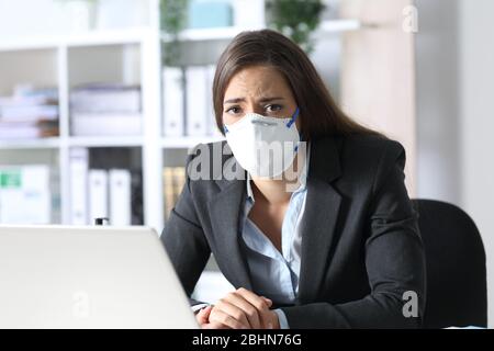 Traurige Exekutive Frau mit Schutzmaske, die auf einem Schreibtisch im Büro auf die Kamera schaut Stockfoto