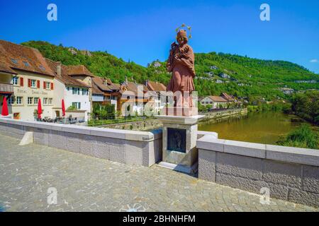 Die Statue Johannes von Nepomuk steht auf halbem Weg auf der Brücke über den Fluss Doubs, Saint Ursanne. Kanton Jura, Schweiz. Stockfoto