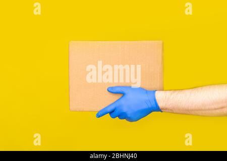 Nahaufnahme Hände Lieferung Mann medizinische Handschuhe halten leere Karton auf gelben Studio Hintergrund. Service Coronavirus. Online-Shopping. Mock up. Stockfoto