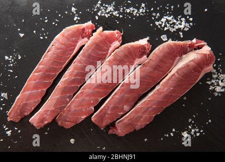 Scheiben von frischem Thunfisch mit grobem Salz auf schwarzem Hintergrund. Stockfoto