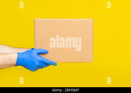 Nahaufnahme Hände Lieferung Mann medizinische Handschuhe halten leere Karton auf gelben Studio Hintergrund. Service Coronavirus. Online-Shopping. Mock up. Stockfoto