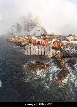 Herrlicher Wintertag in Hamnoy - beliebtes Touristenziel von Lofoten. Spätes Sonnenlicht leuchtet rote Häuser in bewölkten, frostigen Tag. Berge im Hintergrund Stockfoto