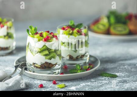 Zwei Gläser gesunde Mahlzeit aus Müsli auf grauem Teller, Joghurt und Kiwi-Früchte. Leckeres Essen zum Frühstück. Traditioneller amerikanischer Snack. Stockfoto