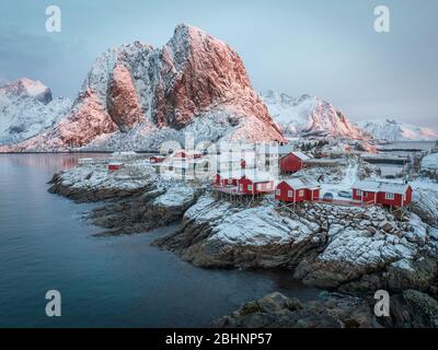 Atemberaubender Sonnenaufgang in Hamnoy - beliebtes Reiseziel. Erstes Licht auf schneebedeckten Bergen und roten traditionellen Häusern im Fischerdorf. Kalter Sieg Stockfoto