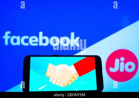 Jaipur, Indien, um 2020 - Foto eines Mobiltelefones mit einem Handschlag, was einen Deal bedeutet, mit facebook und Reliance jio im Hintergrund Stockfoto