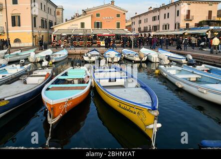 Blick auf Bardolino vom Hafen am Ufer des Gardasees mit bunten Fischerbooten, einem kleinen Zug und Wanderern, Verona, Venetien, Italien Stockfoto