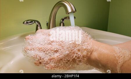 Frau wäscht sich während der Coronavirus-Quarantäne in einem grünen Bad mit Wasser und Seife die Hände. Stockfoto