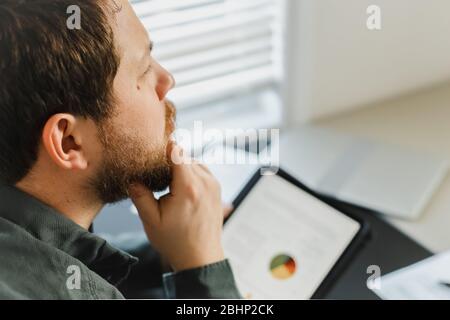 Closeup Finanzier denken mit Tablet und Blick auf Grafiken mit Diagrammen auf dem Bildschirm. Stockfoto
