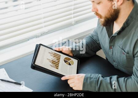 Geschäftsmann arbeitet mit Grafiken und Diagrammen auf Tablet im Büro. Stockfoto