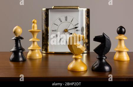 Zwei Ritter stehen einander auf einem Holztisch gegenüber, mit einem Wecker und anderen Schachfiguren im Hintergrund Stockfoto