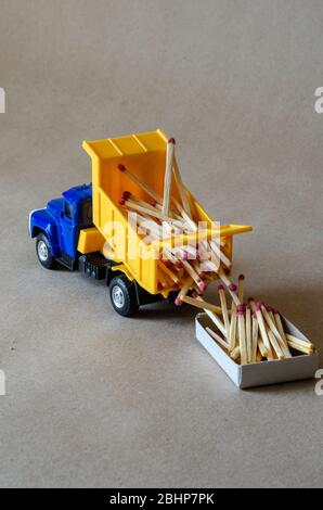 Ein gelber Kipper mit einem blauen Fahrerhaus trägt Streichhölzer. Spielzeugwagen mit einem ganzen Körper aus Holz Streichhölzer. Kreativer industrieller Hintergrund. Protokollierung und Logisti Stockfoto