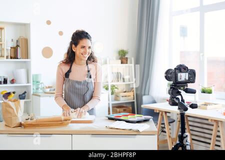 Lächelnde junge Frau Kneten Teig für Cupcakes während der Aufnahme Video für ihre Lebensmittel-Blog Stockfoto