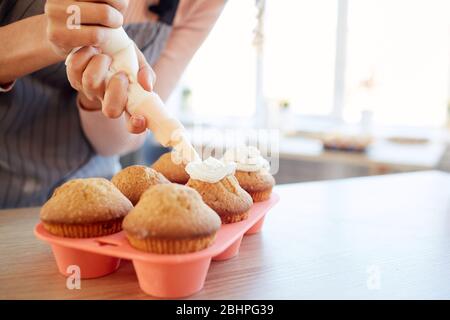Horizontale Nahaufnahme von unkenntlich erkennbaren jungen Frau, die hausgemachte Cupcakes mit Buttercreme dekorieren Stockfoto